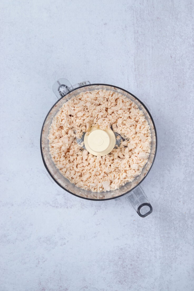 Cooked chicken perfectly chopped inside a food processor work bowl.