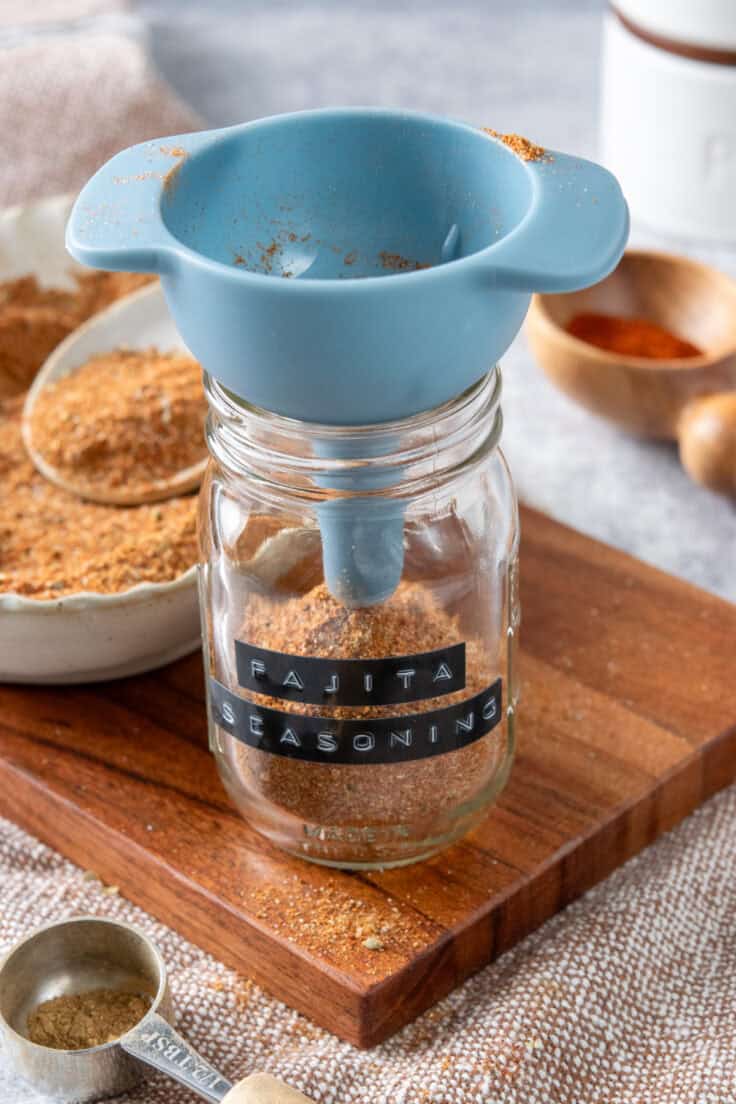 Pouring homemade fajita seasoning into a spice jar using a funnel.