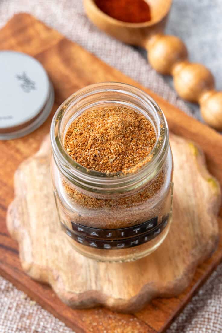 Close-up of homemade fajita seasoning in a spice jar showing oregano flakes and spice blend texture.
