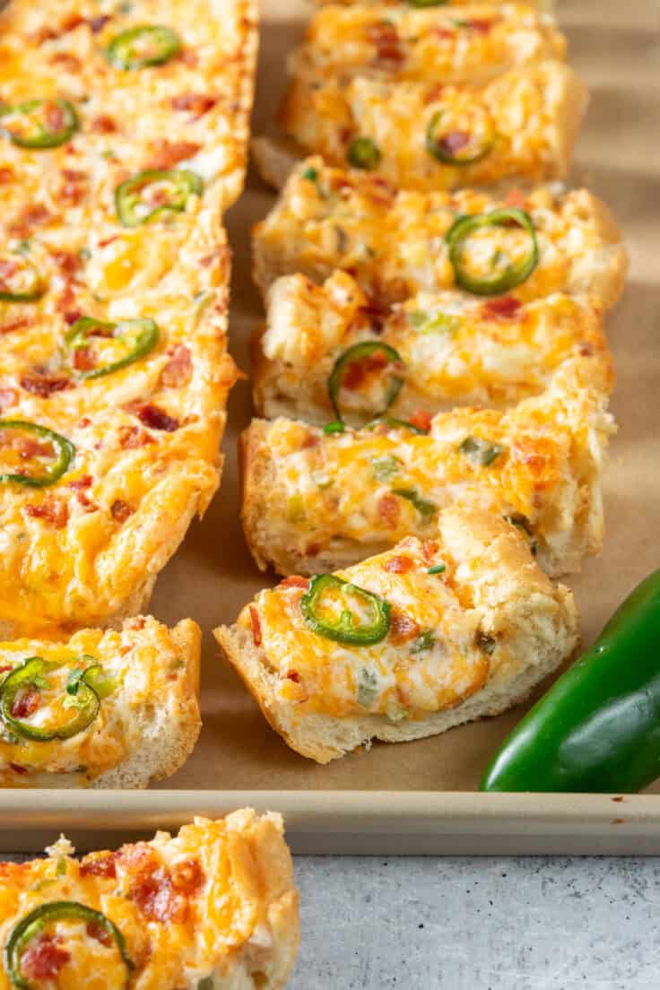 Jalapeño popper cheese bread on a baking tray with one loaf sliced and a whole fresh jalapeño in front.