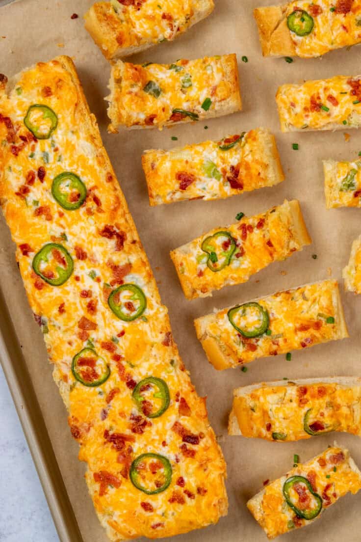 Overhead view of jalapeño popper cheese bread on a baking tray, with one sliced for serving.