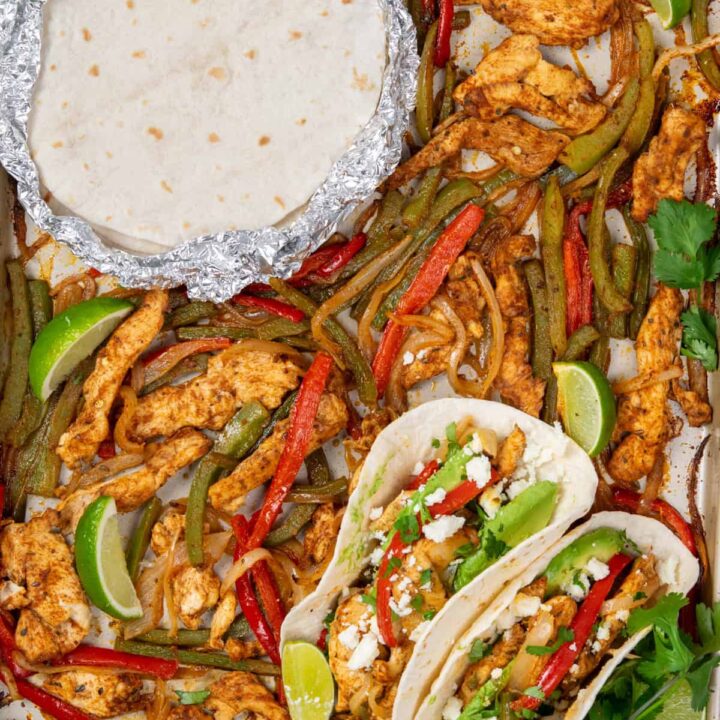 Sheet pan chicken fajitas just out of the oven with roasted chicken, peppers, and onions, foil-wrapped tortillas, and assembled fajitas with toppings and lime.