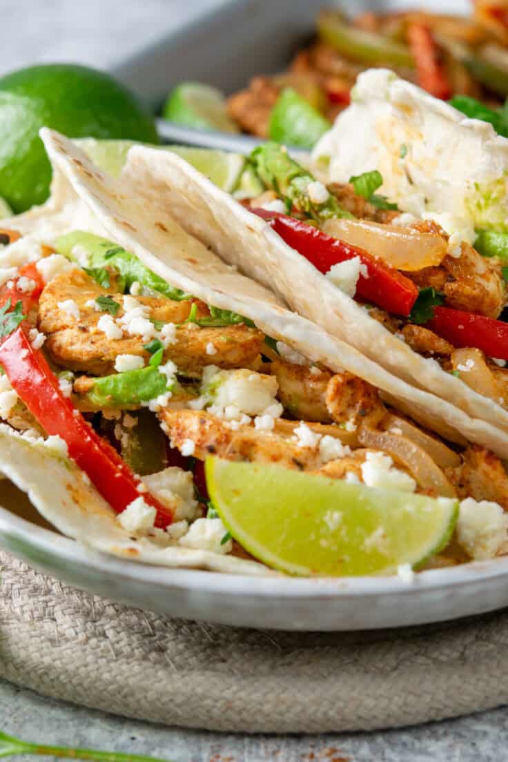 Close-up of a chicken fajita with seared seasoned chicken, avocado, fresco cheese, cilantro, and a lime wedge.