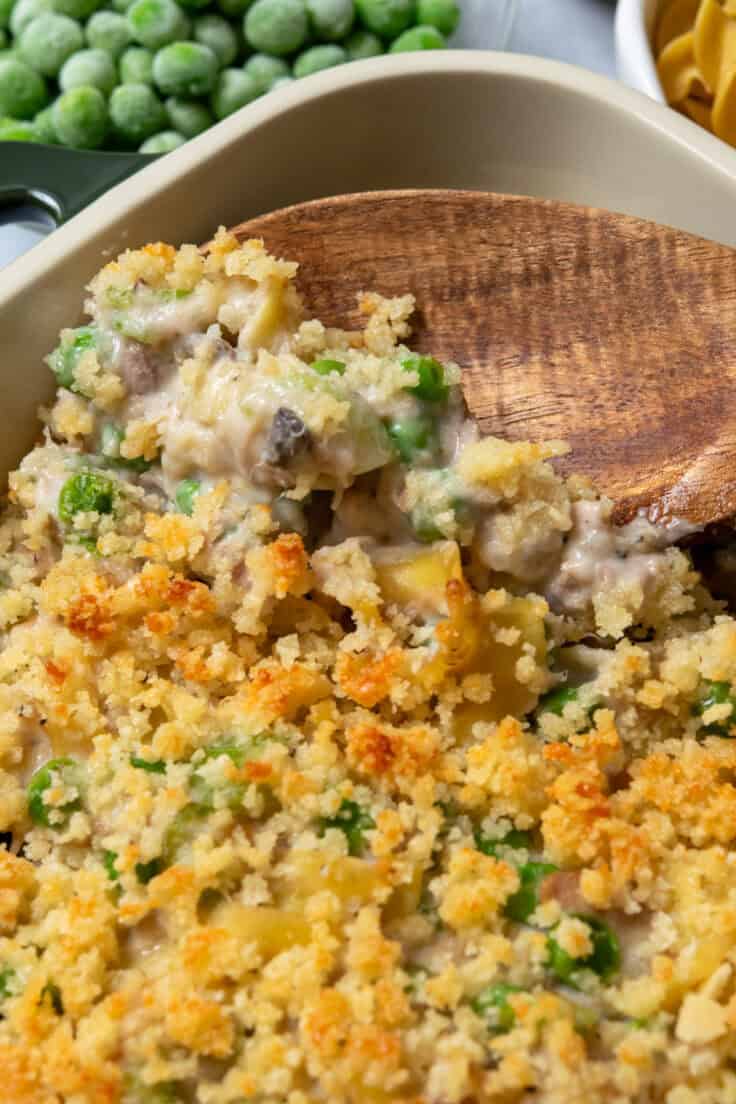 Serving spoon lifting creamy tuna noodle casserole with egg noodles, peas, and flaky tuna.