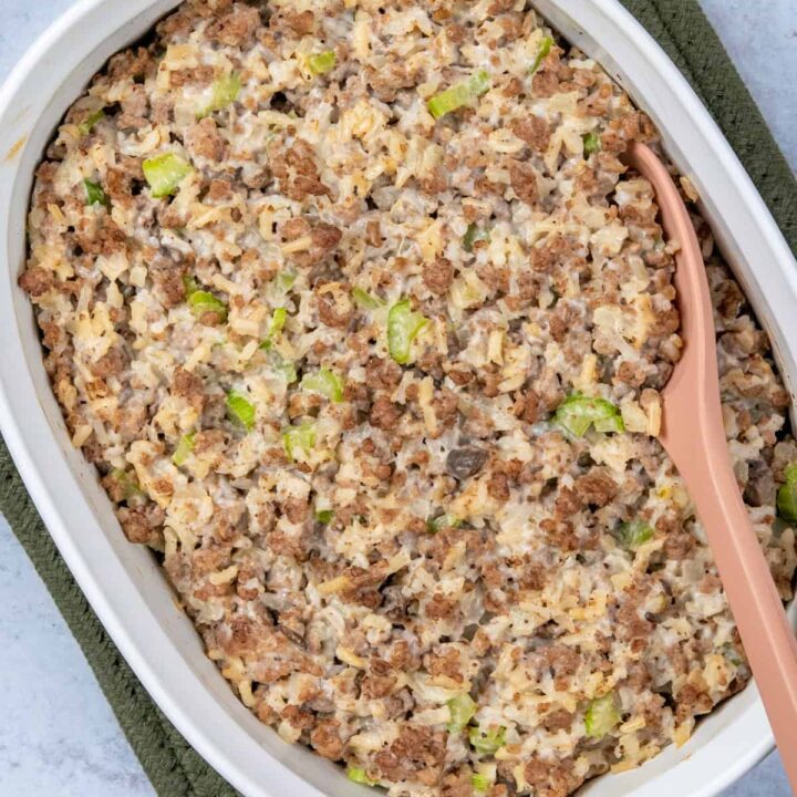 A white casserole dish filled with baked hamburger and rice casserole, made with cream of mushroom soup, with a serving spoon scooping out a portion.