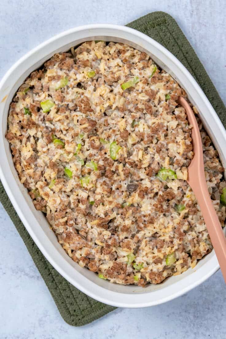 A white casserole dish filled with baked hamburger and rice casserole, made with cream of mushroom soup, with a serving spoon scooping out a portion.