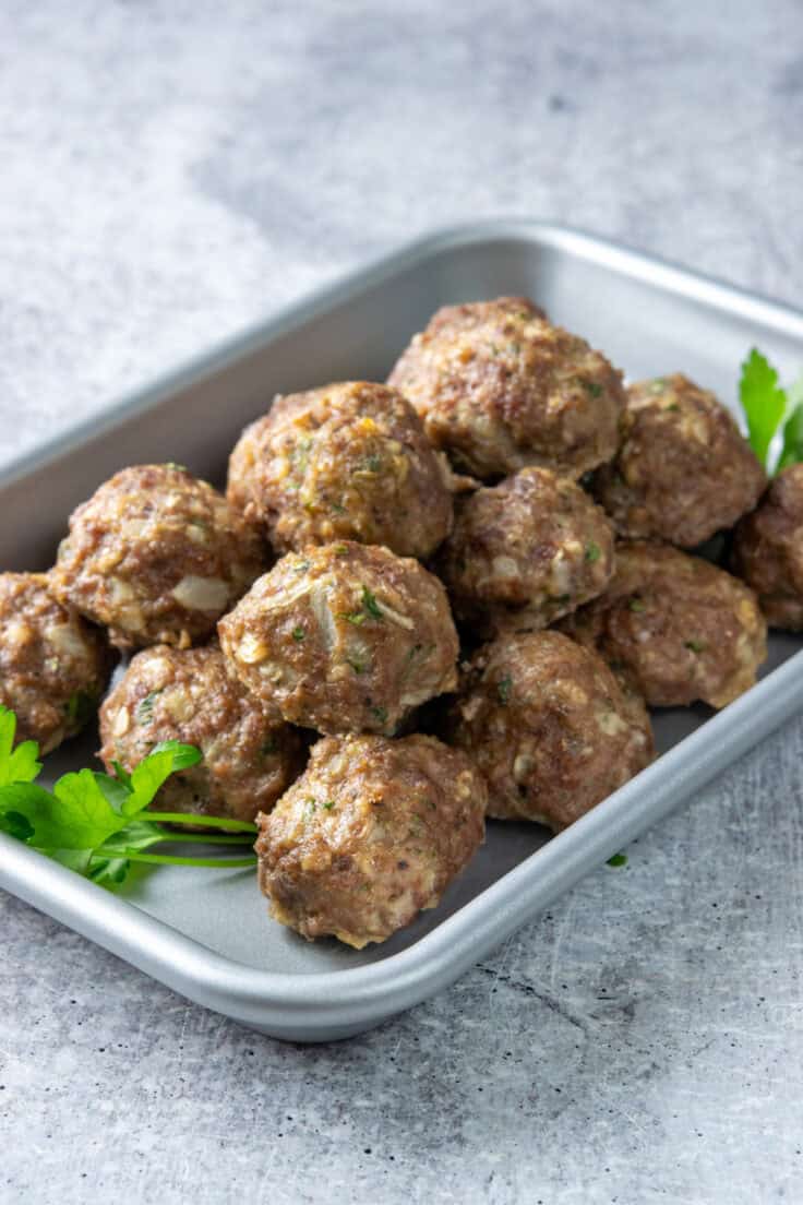 Tray filled with homemade oven-baked meatballs piled together, showing their juicy and tender texture.