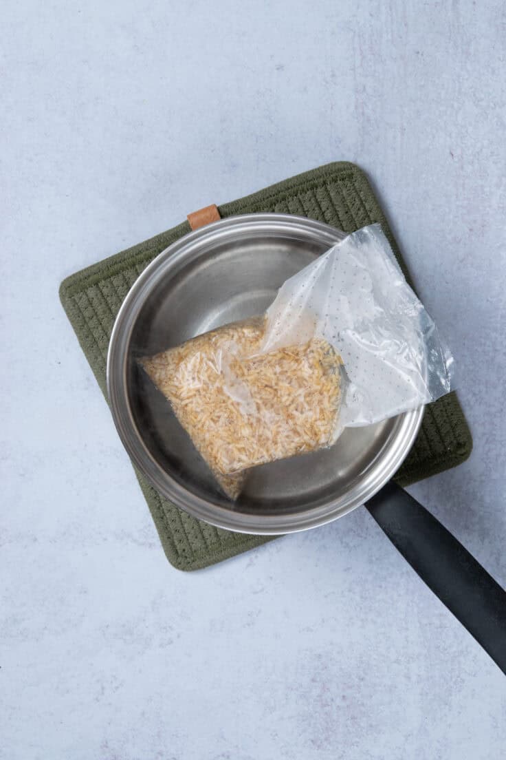 A bag of boil-in-bag brown rice being cooked in a saucepan of boiling water on the stove.