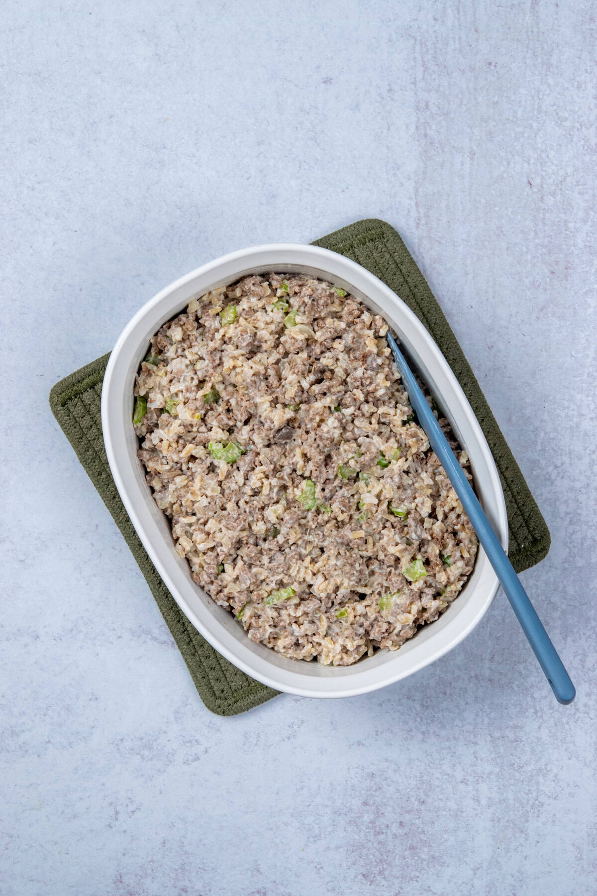 Ground beef, rice, and cream of mushroom soup stirred together in a casserole dish before baking.