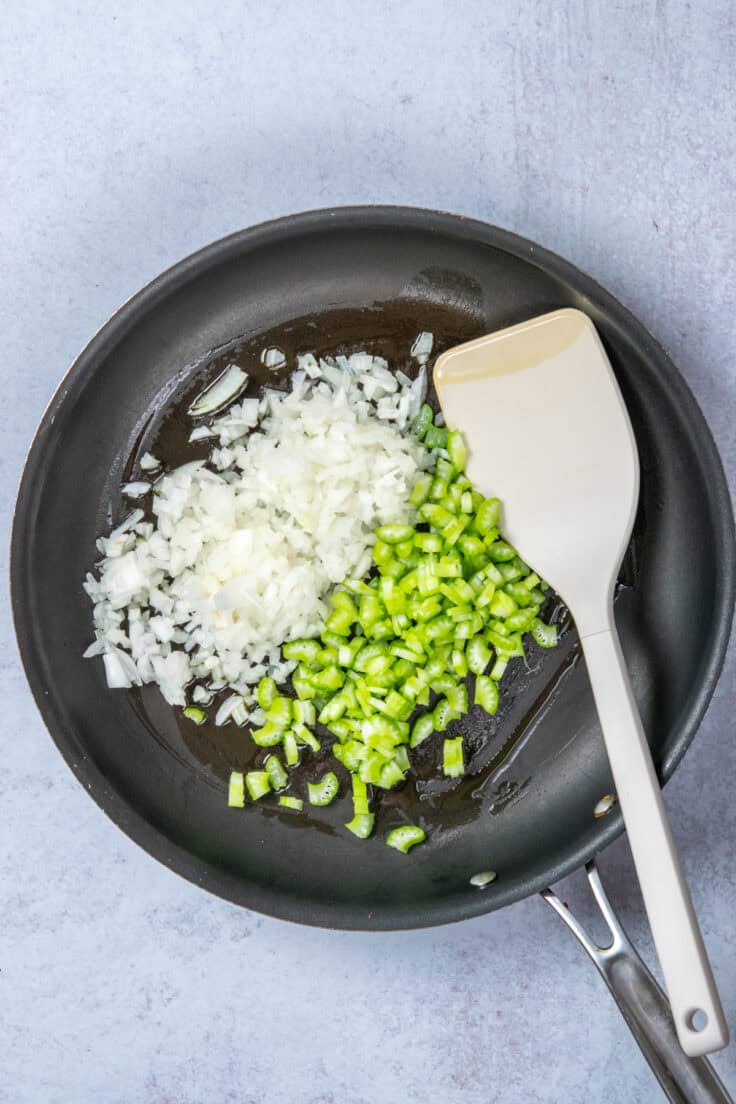 Diced raw onions and celery added to a skillet with olive oil, ready to be sautéed.