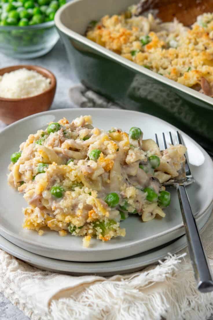 Serving of classic tuna noodle casserole on plate with fork beside baking dish.