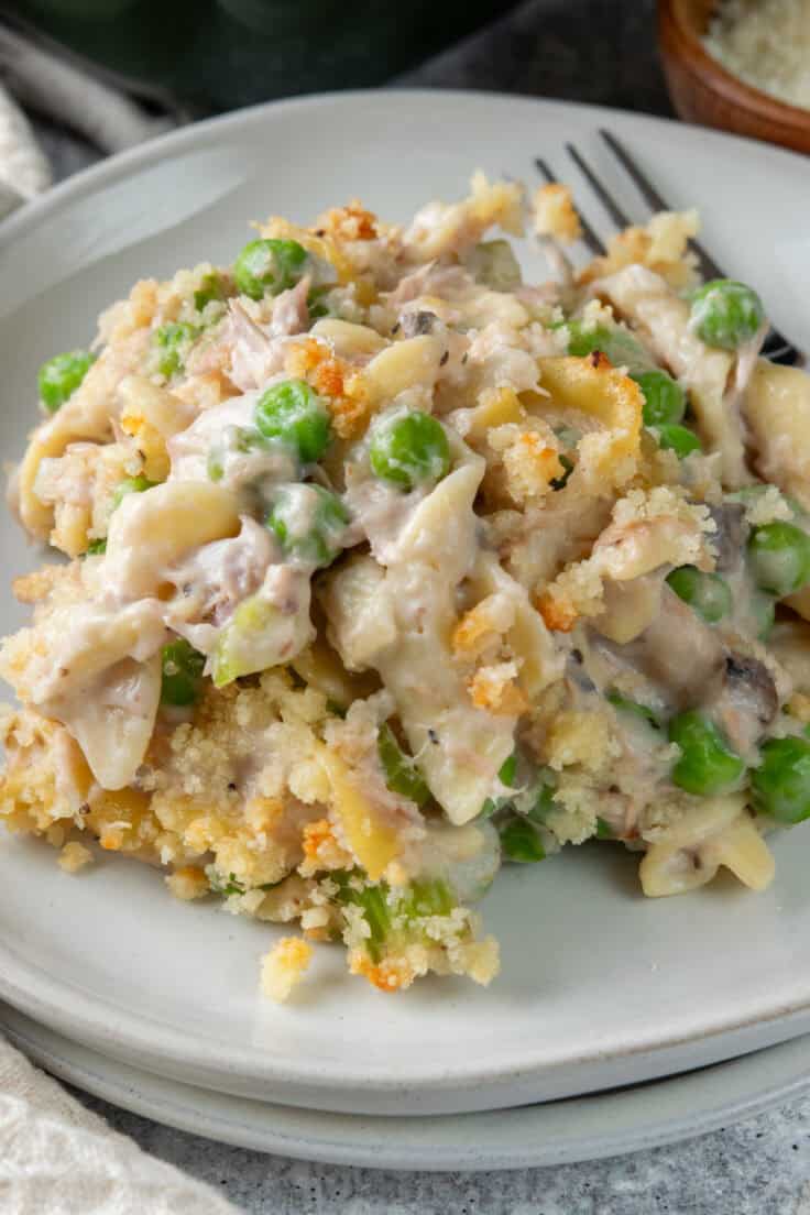 Close-up of creamy tuna noodle casserole with egg noodles, peas, and buttery Parmesan topping.