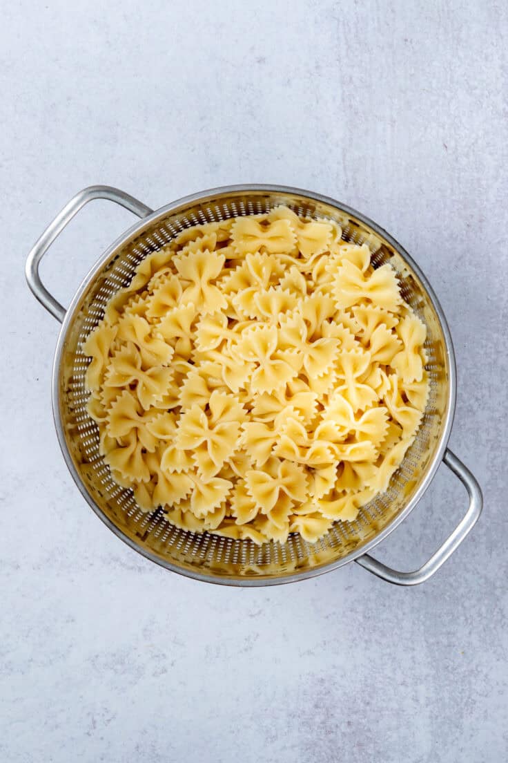 Cooked farfalle pasta draining in a strainer after being rinsed with cold water.