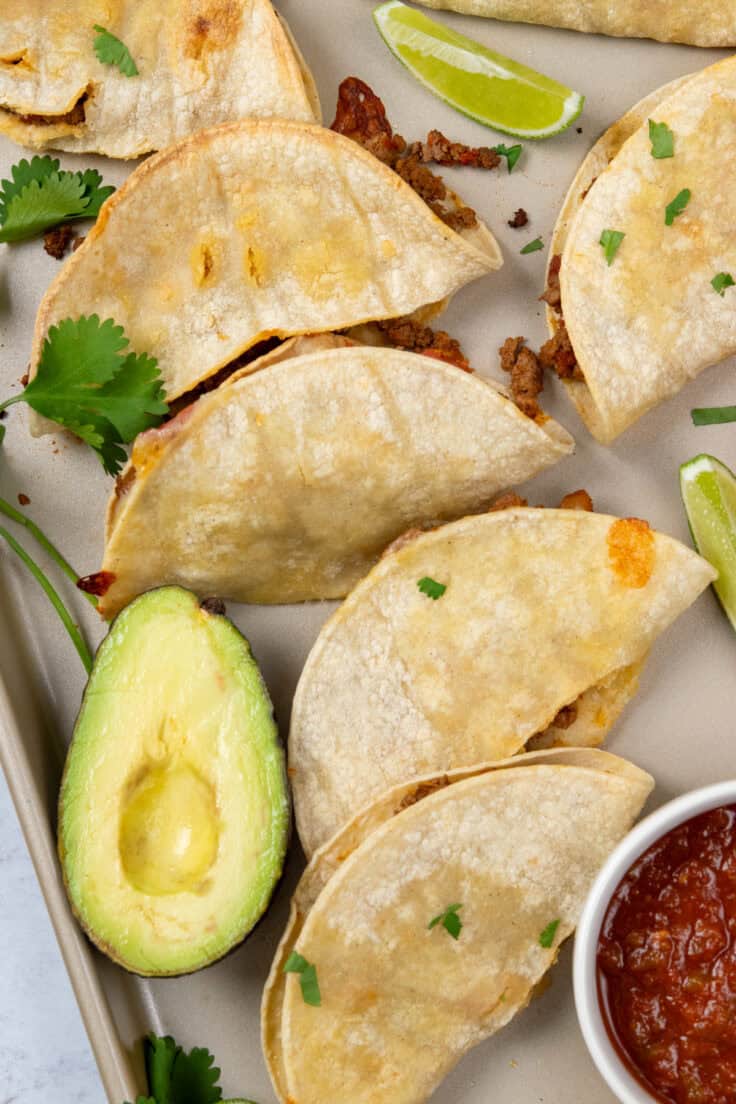 Crispy baked corn tortilla tacos with ground beef and melted cheese fresh from the oven on a sheet pan.