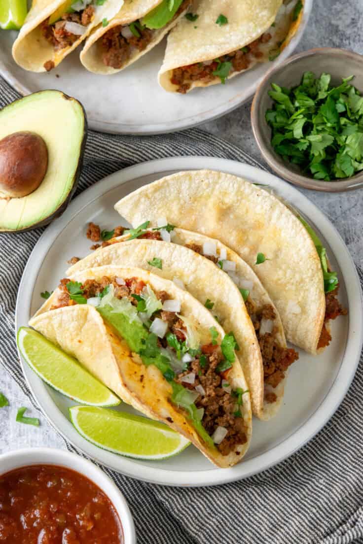 Dinner plates filled with crispy baked beef tacos served with chopped cilantro and salsa.