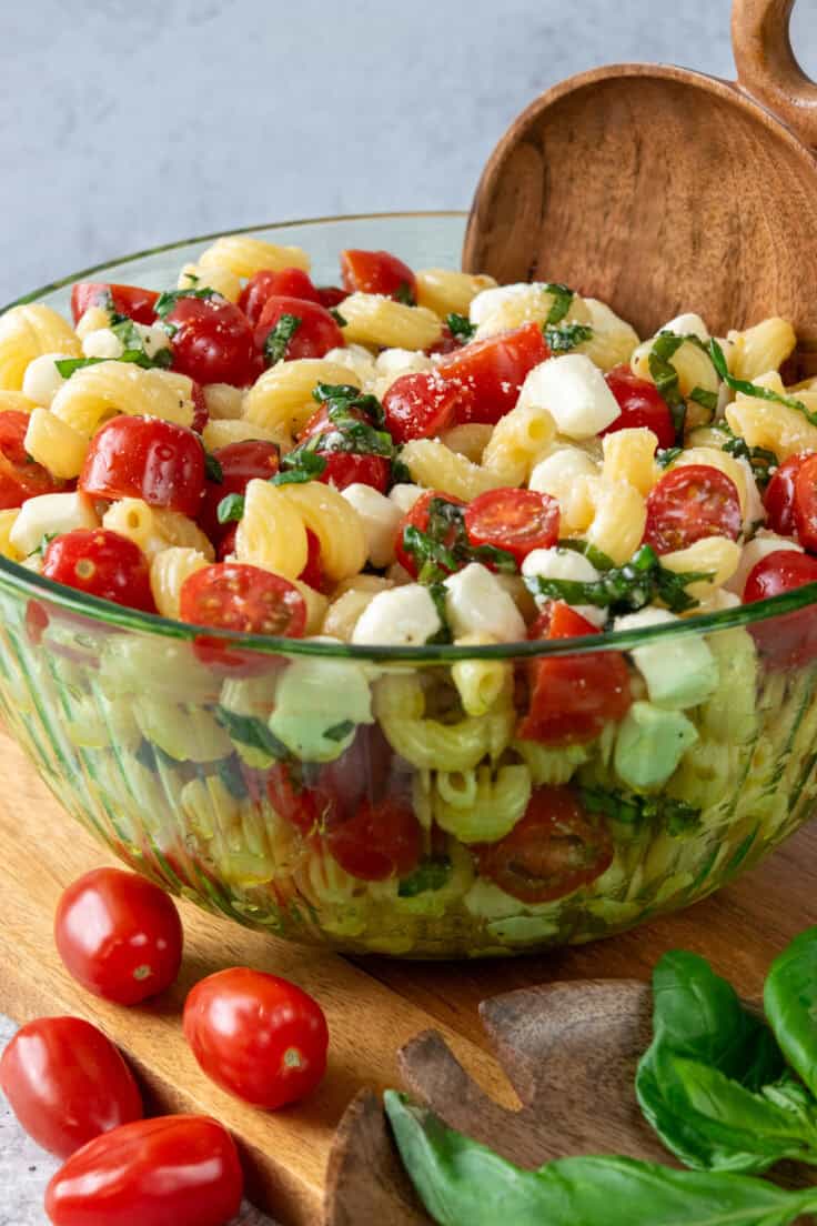 Bowl of caprese pasta salad with tomatoes, cavatappi pasta, mozzarella, basil, vinaigrette, and a sprinkle of parmesan cheese.
