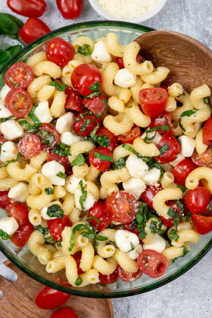 Overhead view of caprese pasta salad with cavatappi pasta, juicy grape tomatoes, pearl mozzarella, and fresh basil tossed in a light vinaigrette.