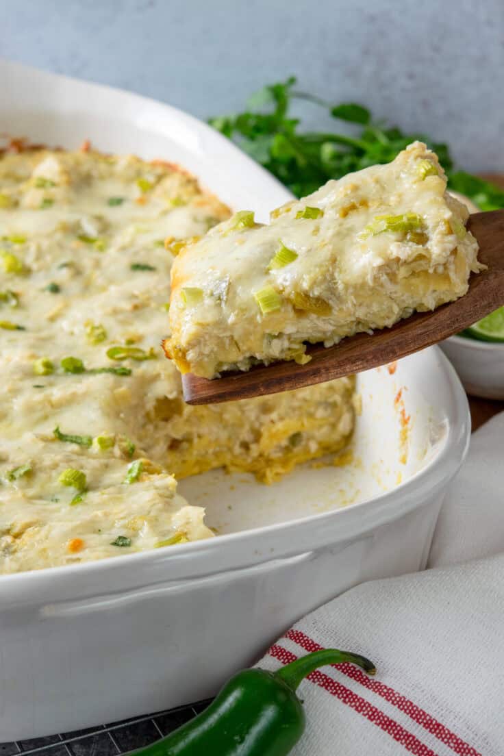 Sliced layered chicken enchilada casserole on a spatula being removed from casserole dish and onto a plate.