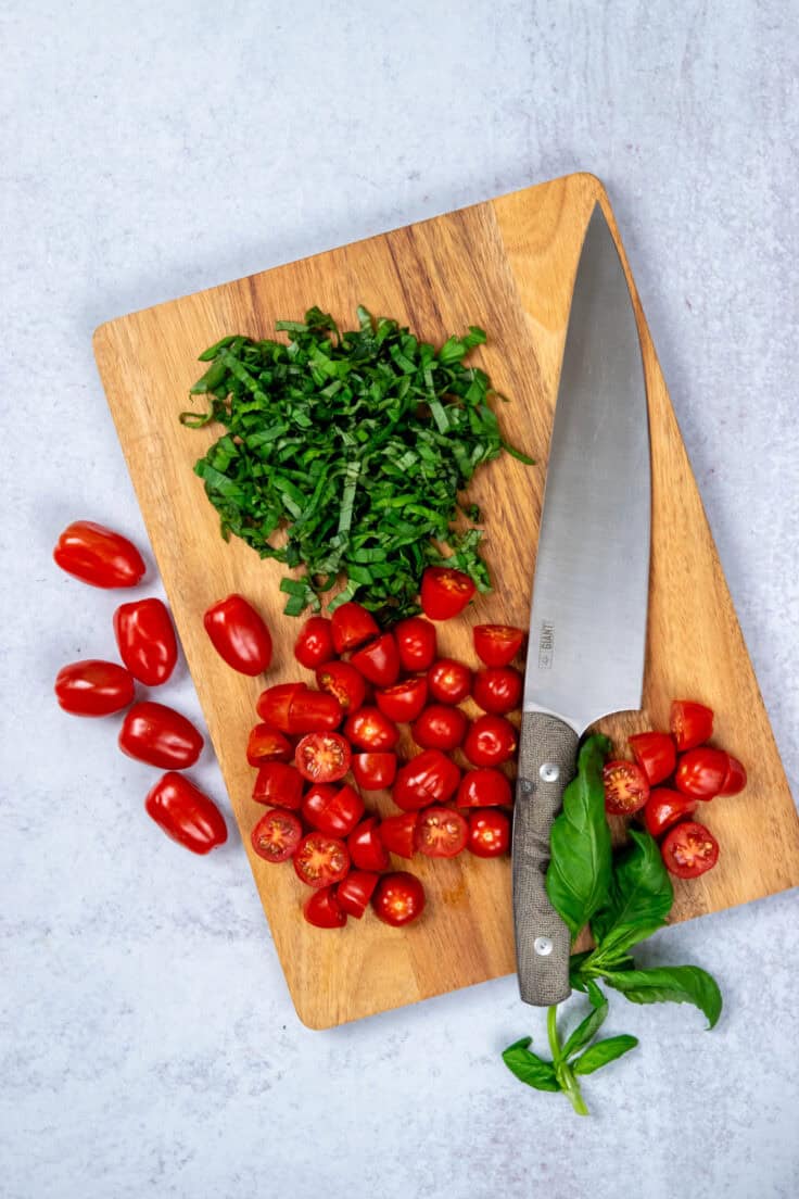 Halved cherry tomatoes, sliced mozzarella balls, and fresh basil prepared for pasta salad.