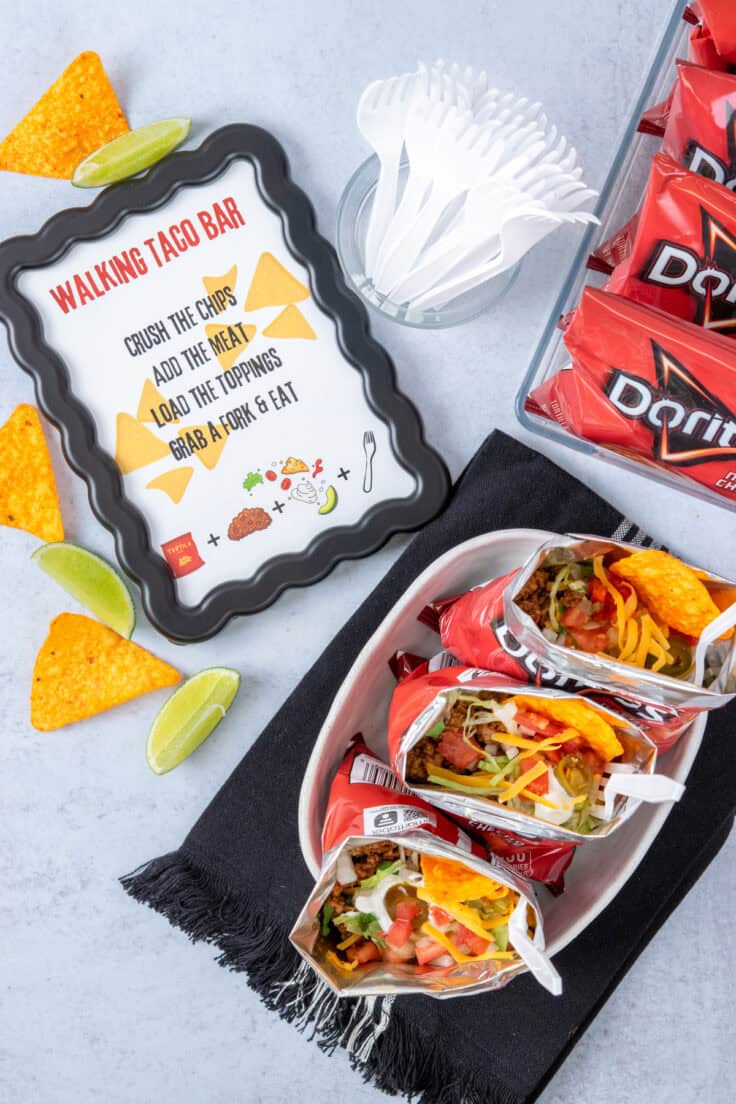 Walking taco bar party setup with a bucket of individual Doritos chip bags alongside prepared walking tacos piled high with meat and toppings.