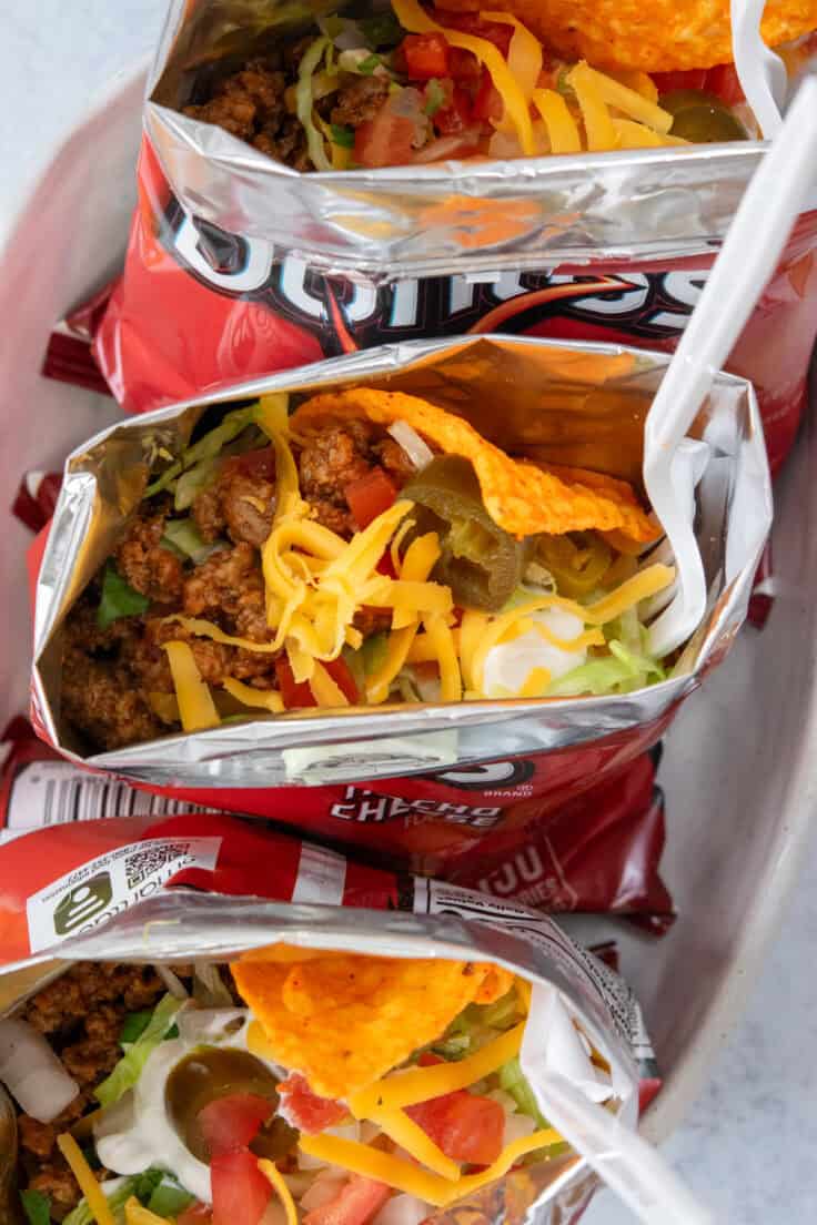 Close-up of a walking taco in a Doritos bag filled with saucy seasoned taco meat, shredded cheddar cheese, lettuce, pico de gallo, jalapenos, sour cream, and crunchy chips.