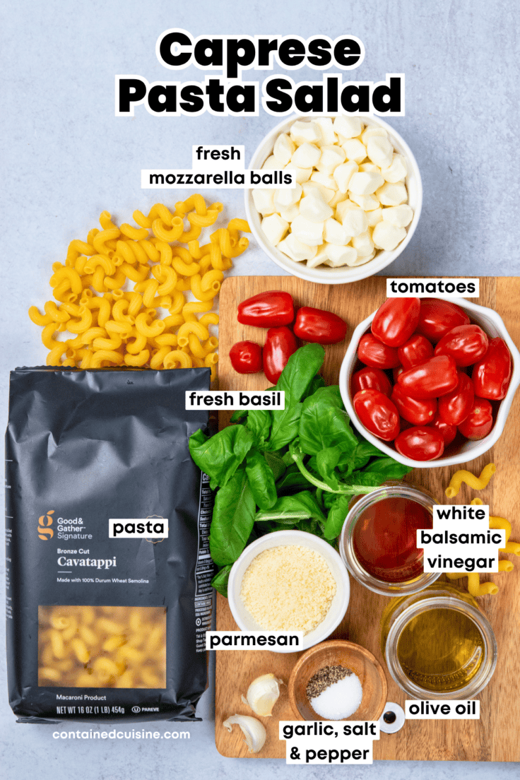 Overhead view of labeled ingredients for caprese pasta salad including pasta, tomatoes, mozzarella, basil, olive oil, vinegar, parmesan and garlic cloves.