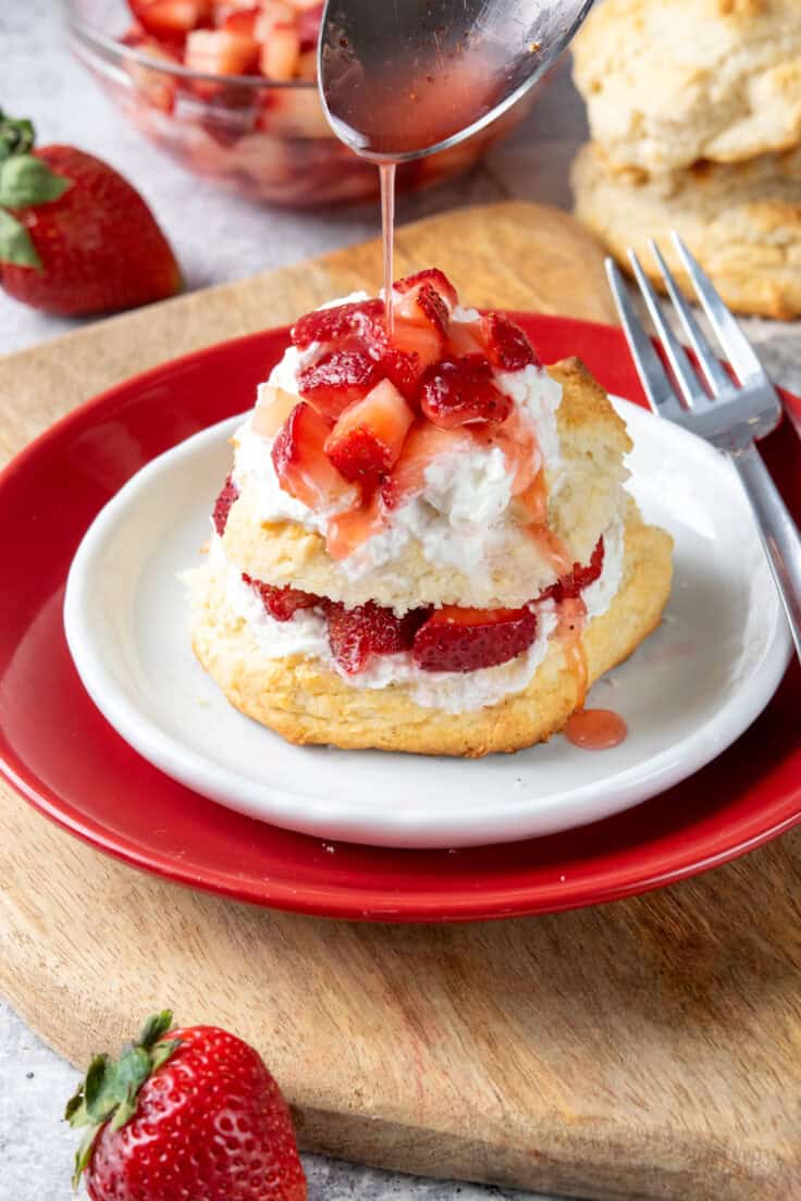 Spoon drizzling sweet strawberry syrup from macerated strawberries over a freshly assembled Bisquick strawberry shortcake.
