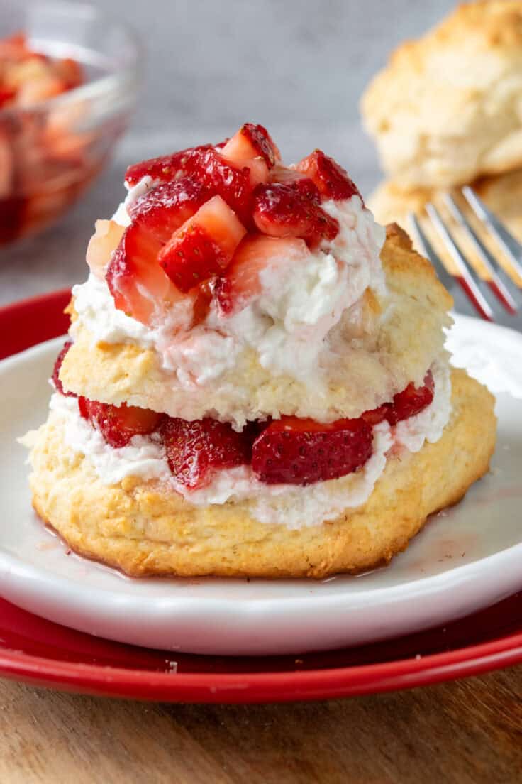 Close-up of a Bisquick strawberry shortcake on a dessert plate with whipped cream, juicy strawberries, and strawberry syrup soaking into the buttery biscuit.
