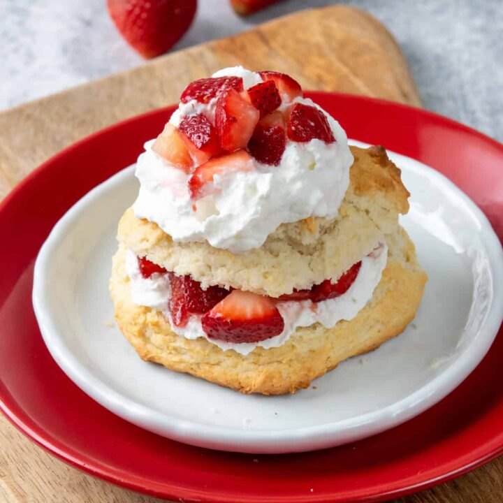 Bisquick strawberry shortcake layered with fluffy whipped cream and juicy strawberries on a buttery biscuit shortcake served on a dessert plate with fresh strawberries beside it.