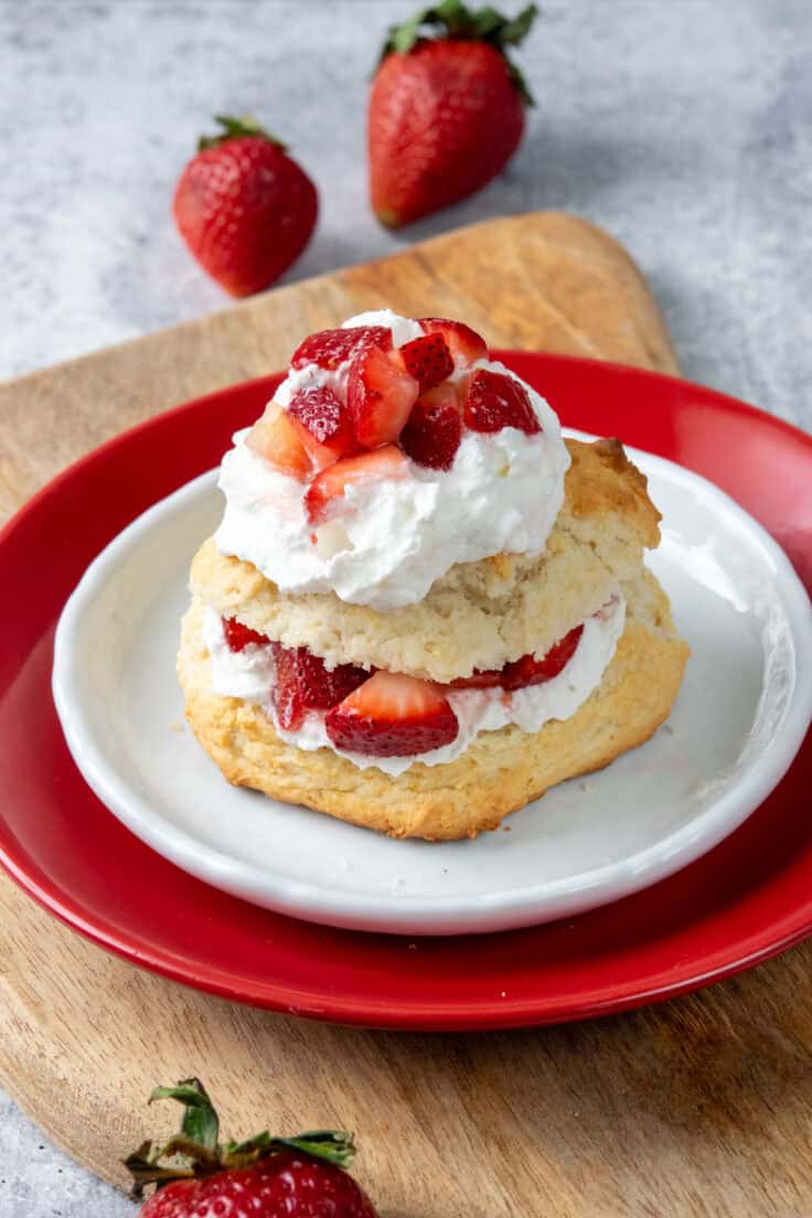 Bisquick strawberry shortcake layered with fluffy whipped cream and juicy strawberries on a buttery biscuit shortcake served on a dessert plate with fresh strawberries beside it.