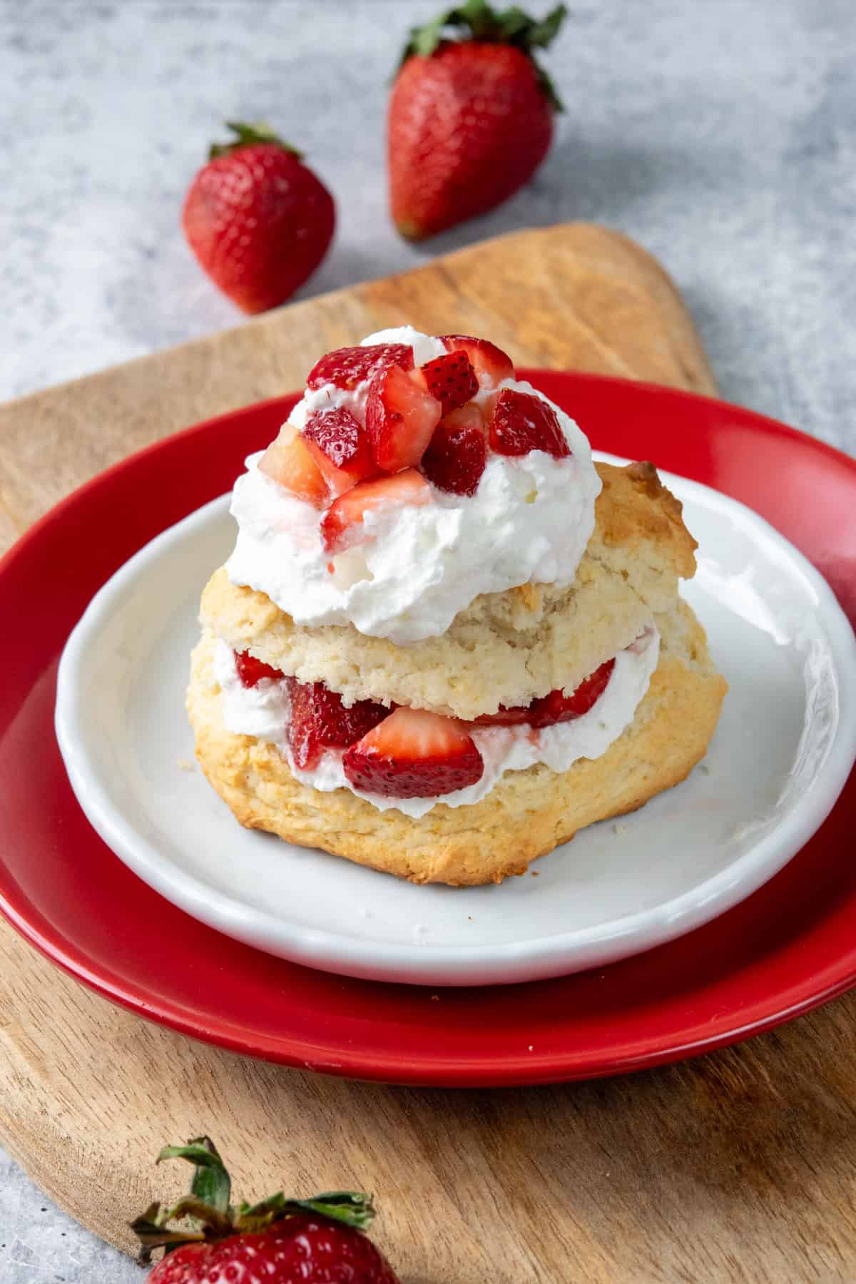 Bisquick strawberry shortcake layered with fluffy whipped cream and juicy strawberries on a buttery biscuit shortcake served on a dessert plate with fresh strawberries beside it.