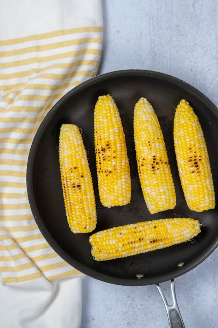 Fresh corn charring in a hot cast iron pan with visible grill marks and deep yellow kernels.