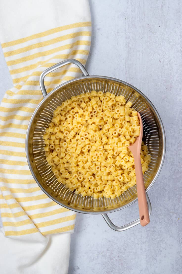 Cooked shell pasta draining in a strainer after being rinsed with cold water to stop cooking.