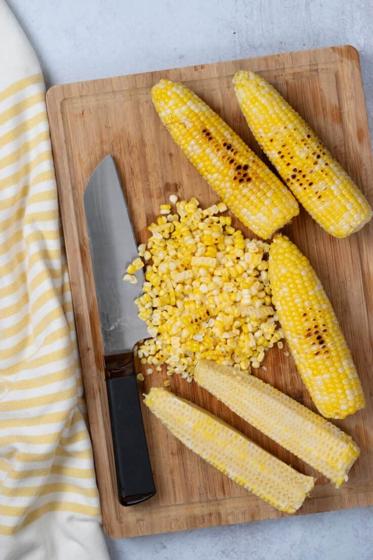 Slicing the roasted corn kernels off ears of corn.