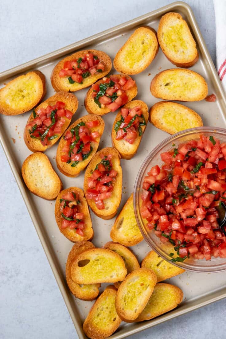 Tomato bruschetta topping being spooned onto toasted garlic bread.