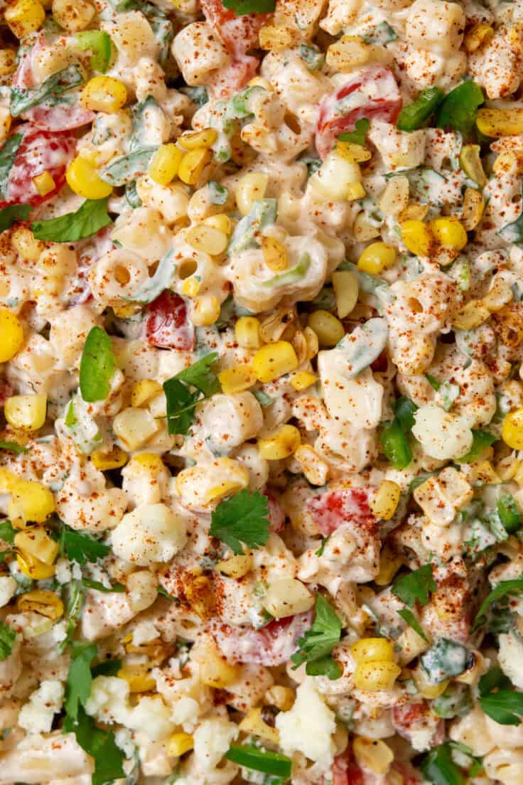 Overhead view of Mexican street corn pasta salad showing ditalini pasta, charred corn, tomatoes, jalapeño, cilantro, and cotija cheese in a creamy lime dressing with a sprinkle of chili powder.