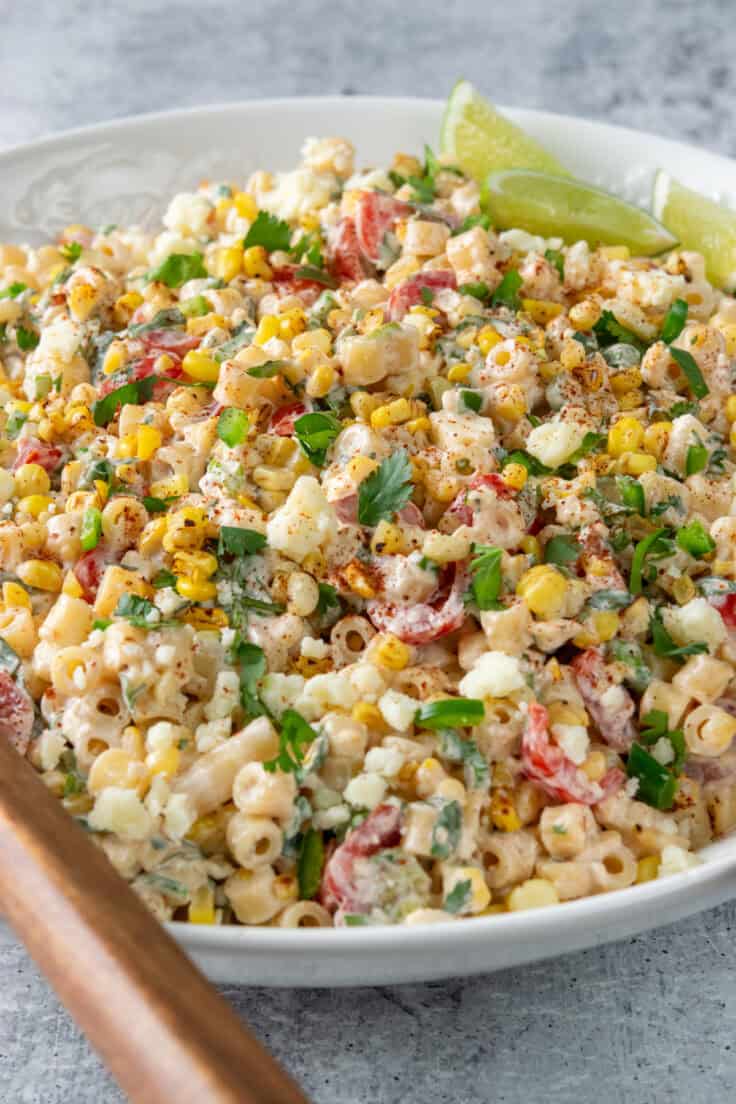Close-up of Mexican street corn pasta salad made with ditalini pasta and coated in a creamy chili lime dressing, with lime wedges tucked into the bowl.