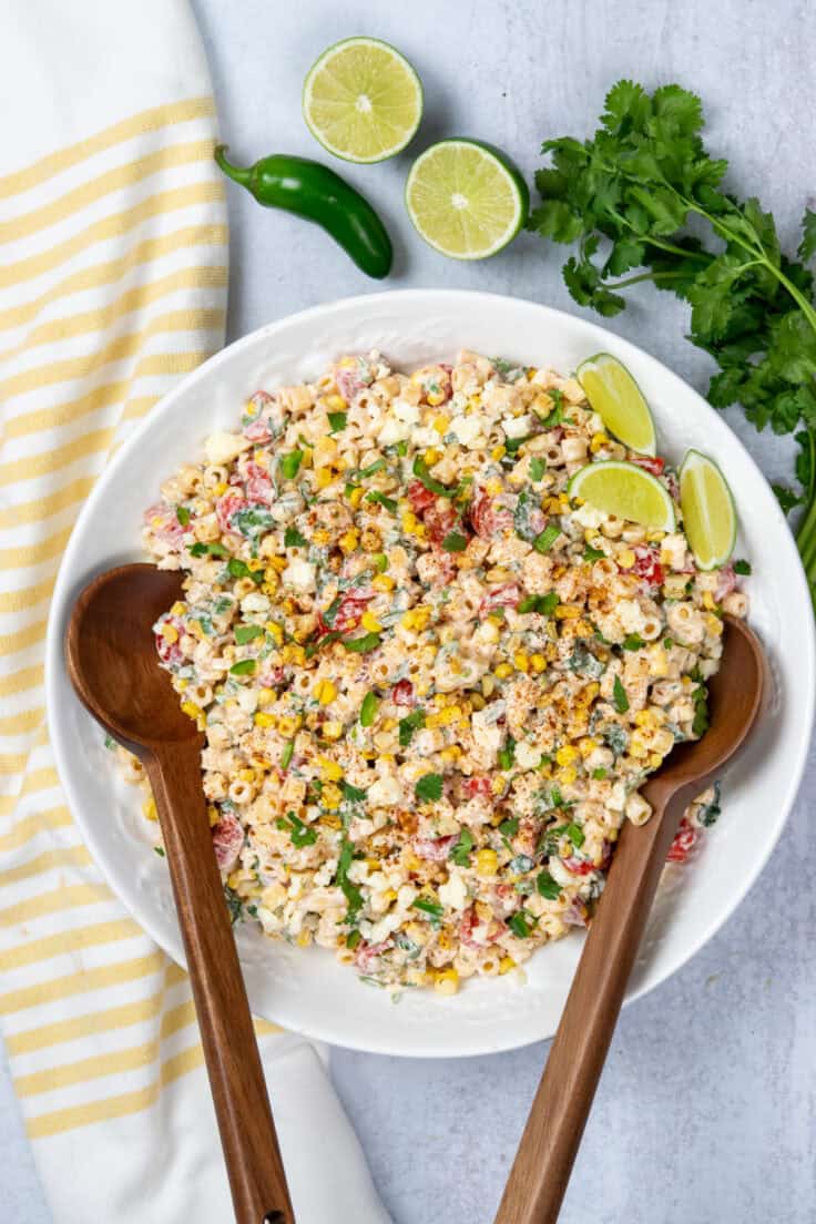 Garnished Mexican street corn pasta salad in a large serving bowl with wood salad spoons.