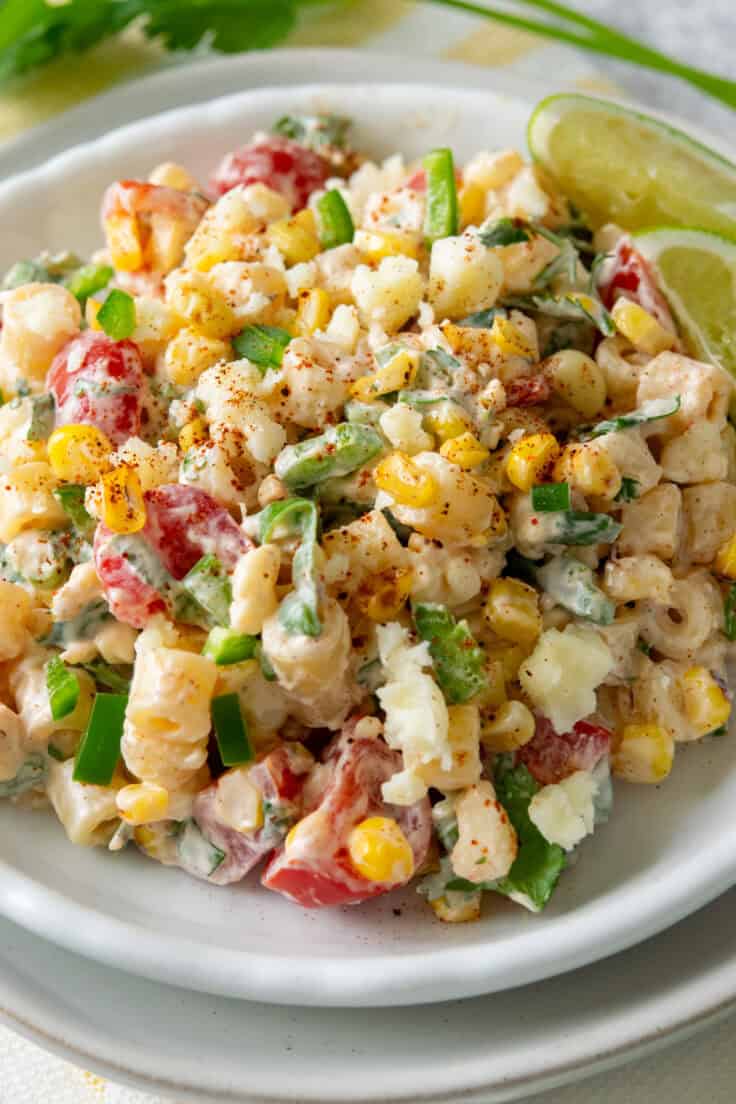 Close-up of Mexican street corn pasta salad on a plate with charred corn, ditalini pasta, tomatoes, cotija cheese, jalapeños, and green onions coated in creamy lime dressing and finished with chili powder.