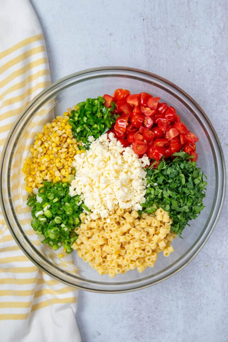 Pasta, corn, vegetables, and cheese arranged in sections in a large mixing bowl before adding dressing.