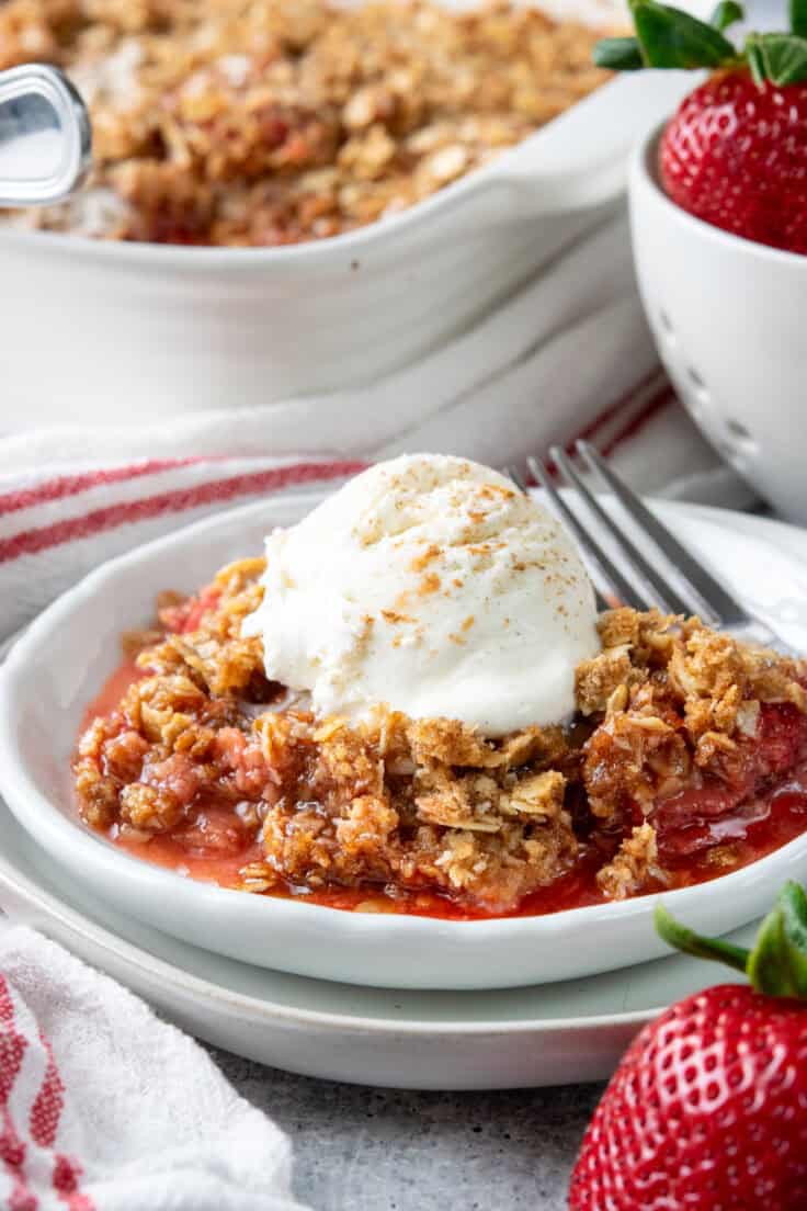Warm strawberry crisp served with melting vanilla ice cream in a dessert bowl.
