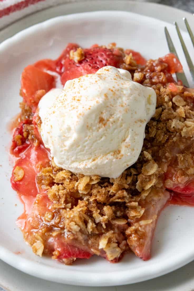 Close-up overhead view of warm strawberry crisp with juicy baked strawberries, buttery oat crumble topping, and melting vanilla ice cream.