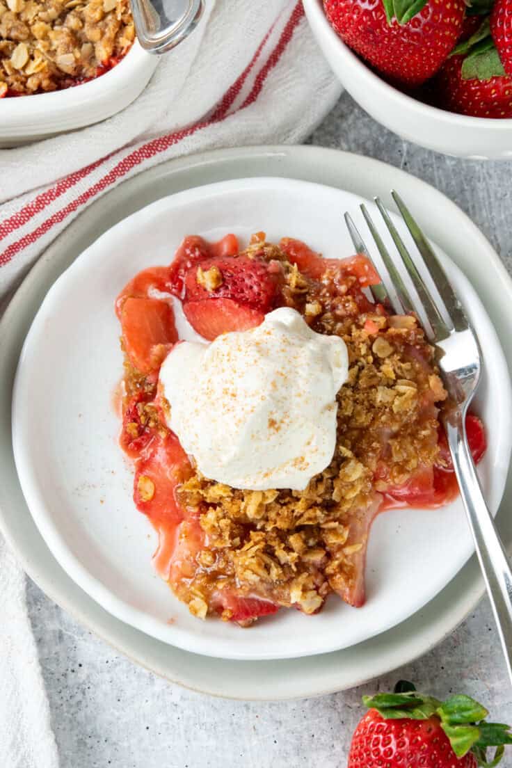 Overhead view of homemade strawberry crisp with a buttery oat crumble topping and melting vanilla ice cream served beside the baking dish filled with the warm summer dessert.