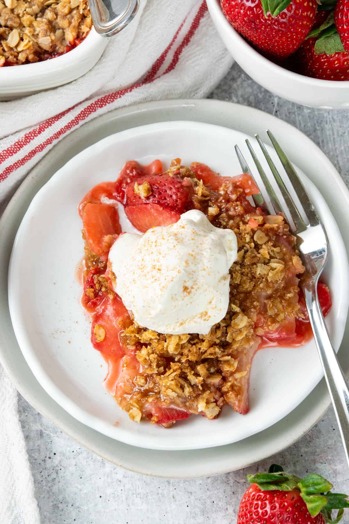 Overhead view of homemade strawberry crisp with a buttery oat crumble topping and melting vanilla ice cream served beside the baking dish filled with the warm summer dessert.