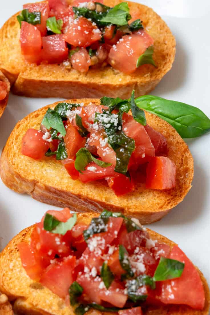 Close-up of classic tomato bruschetta topped with juicy tomatoes, fresh basil ribbons, and olive oil dripping over crisp toasted bread.