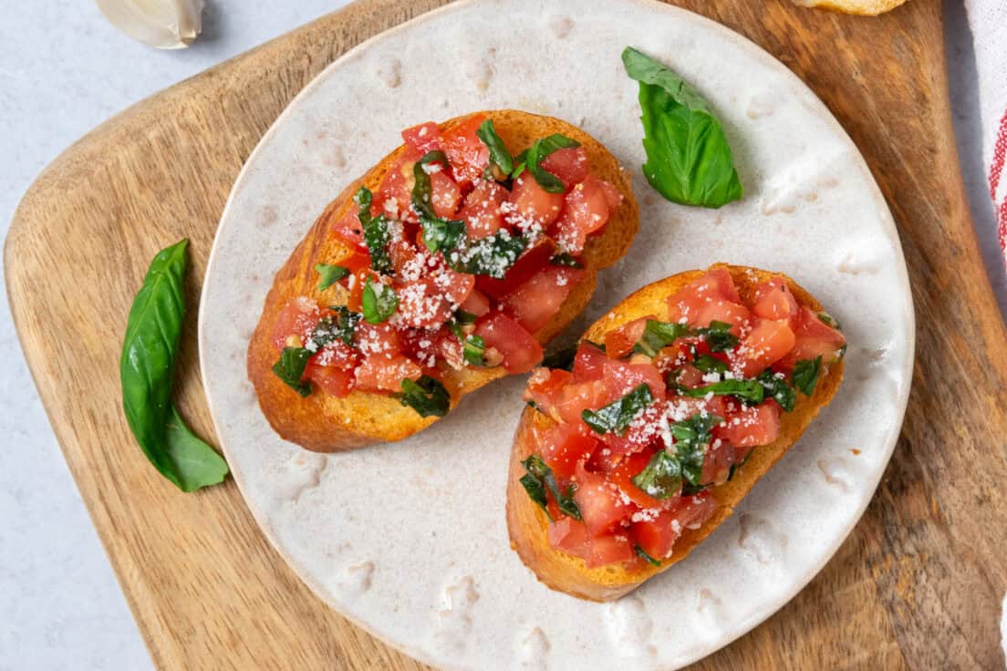 Crispy garlic-rubbed bruschetta toast brushed with olive oil and topped with fresh tomato and basil mixture on a small plate.