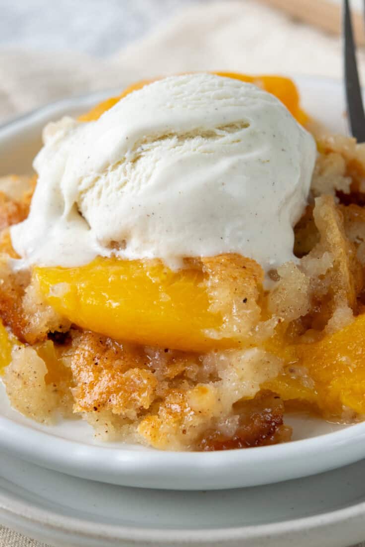 Close-up of warm Bisquick peach cobbler topped with melting ice cream, highlighting the buttery cobbler and juicy cinnamon-spiced peaches.