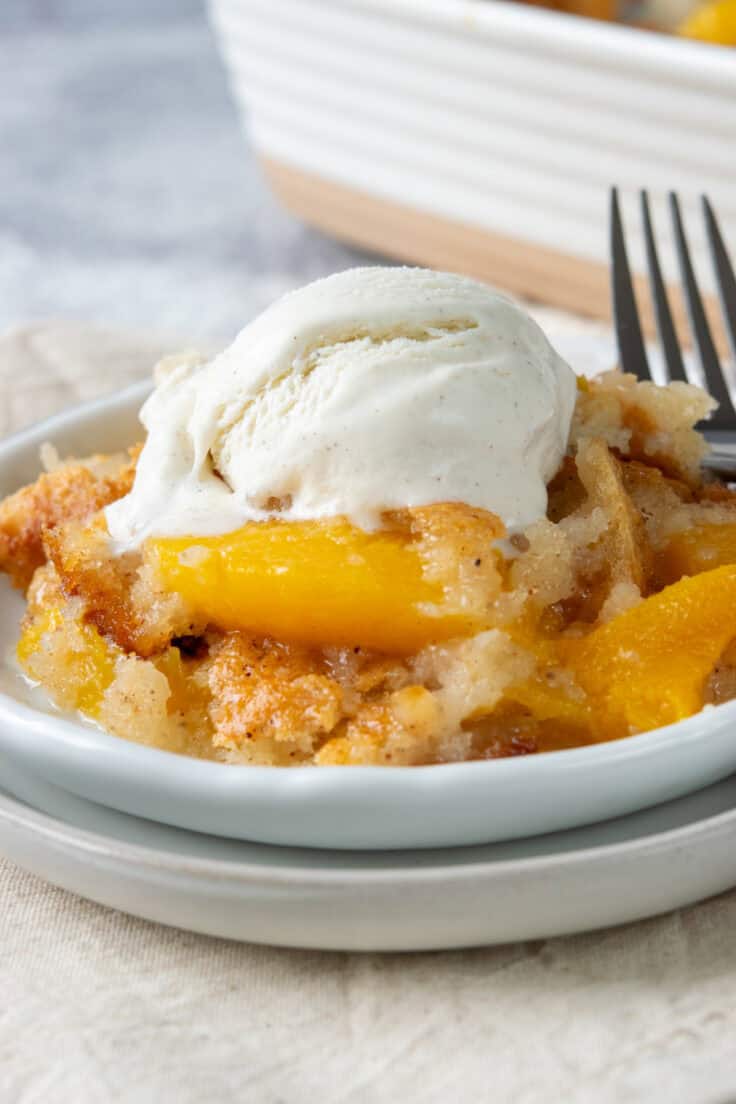 Close-up of Bisquick peach cobbler topped with a large scoop of vanilla ice cream, showing juicy cinnamon-spiced peaches and a moist buttery cobbler.