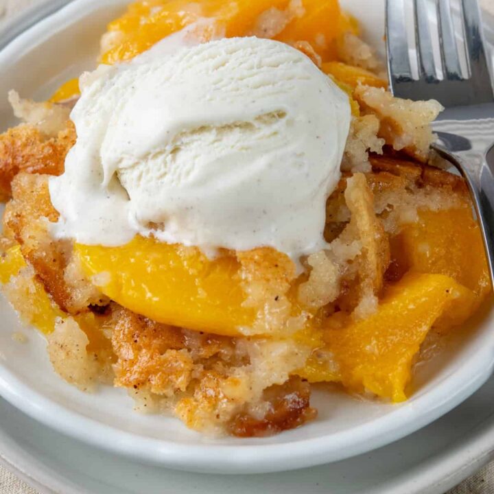 A rich serving of Bisquick peach cobbler topped with melting vanilla ice cream, featuring juicy peaches and a buttery golden cobbler.