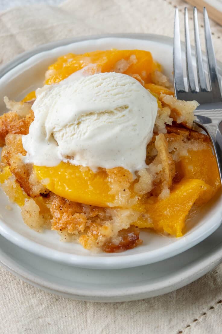 A rich serving of Bisquick peach cobbler topped with melting vanilla ice cream, featuring juicy peaches and a buttery golden cobbler.